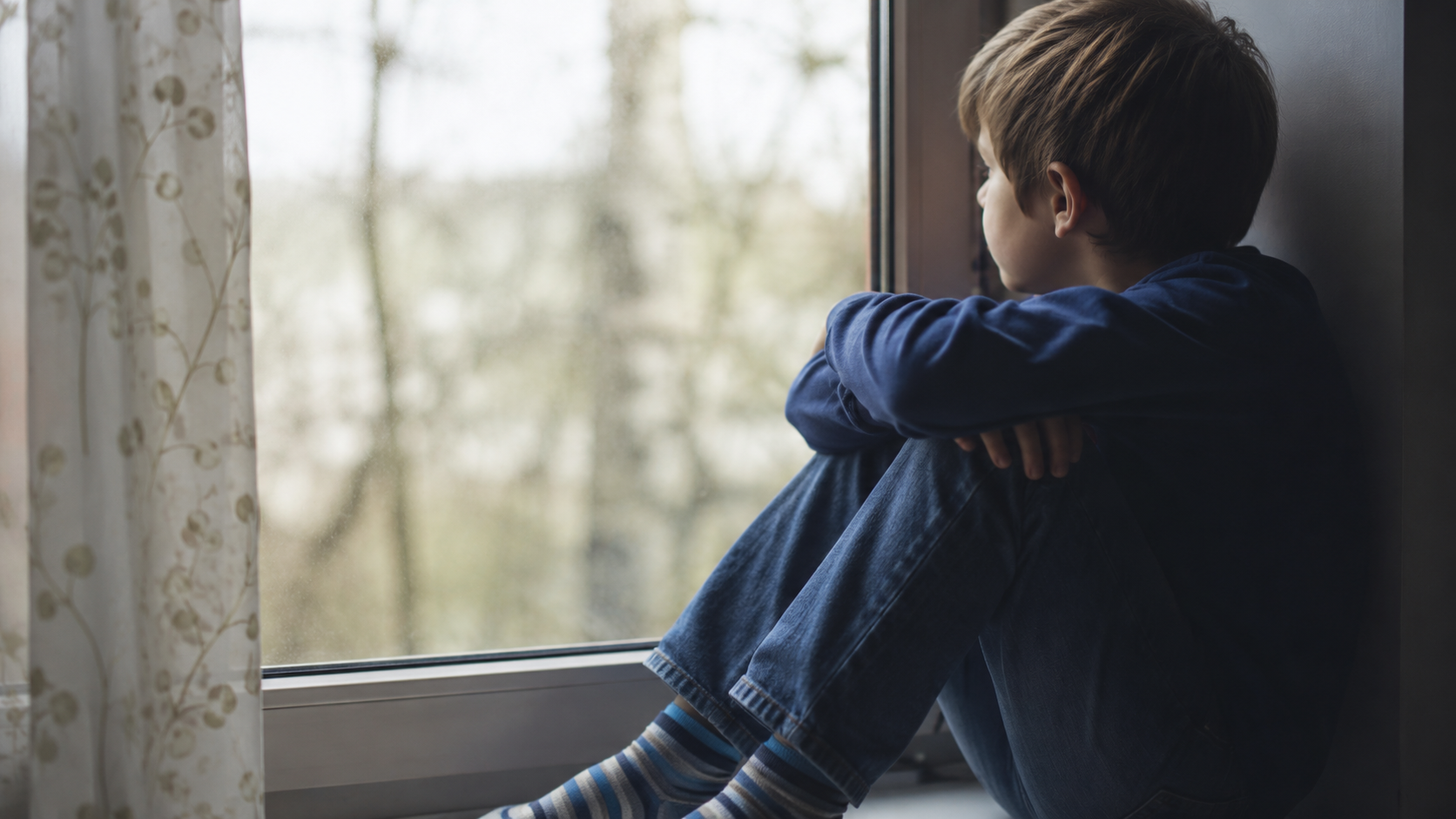 Niño observando el exterior desde una ventana en un momento de reflexión y aislamiento